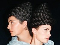 Two people are wrapped together in cloth with matching braids piled on their heads