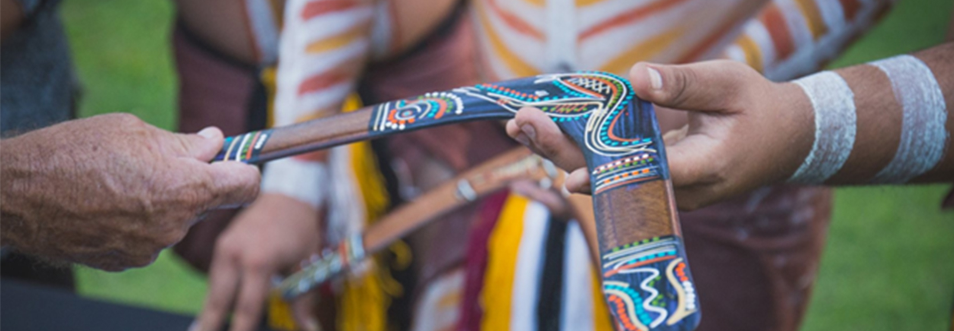 First Nations boomerang with artwork being handed to man