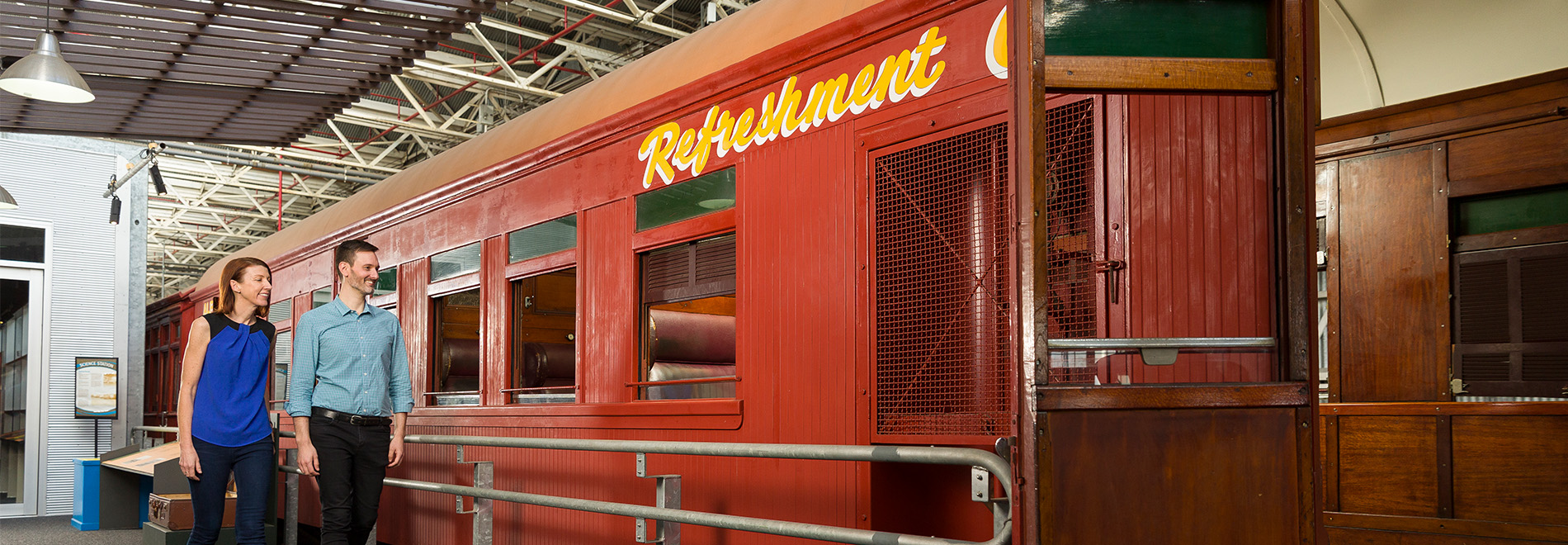 a couple walk beside a red refreshments carriage 